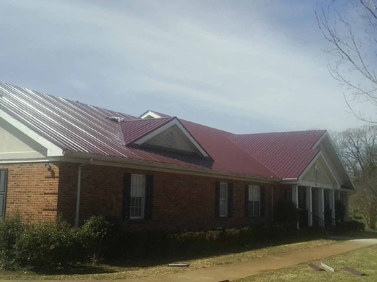 Red metal roof with gabled entries on a long brick building, from a Hail Damage Roof Repair job in Milltown