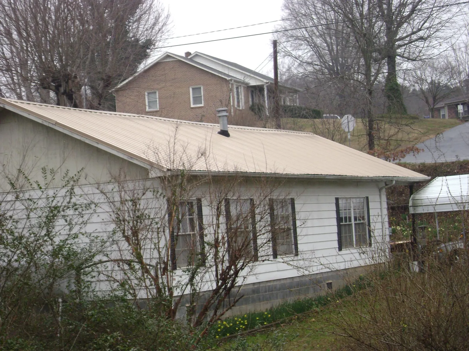 Tan metal roof on a white sided house set into a hillside — Commercial Roofing by Roofing Brothers in Milltown